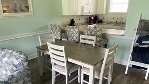 Un comedor con una mesa y sillas de madera, una cocina con armarios blancos y una ventana con persianas.