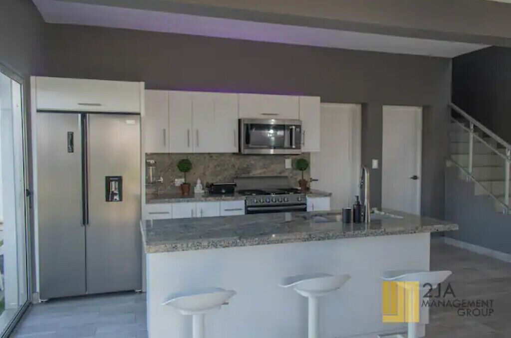 A modern kitchen with white cabinets, a stainless steel refrigerator, a microwave, and a granite countertop.