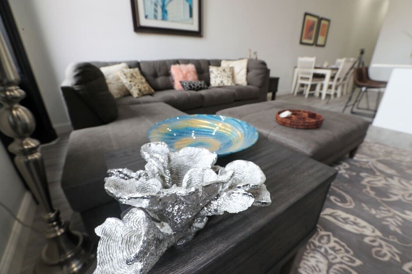 A living room with a grey sofa, a decorative metallic sculpture, and a blue and yellow glass bowl on the coffee table.