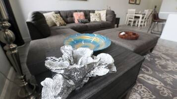 A living room with a grey sofa, a decorative metallic sculpture, and a blue and yellow glass bowl on the coffee table.