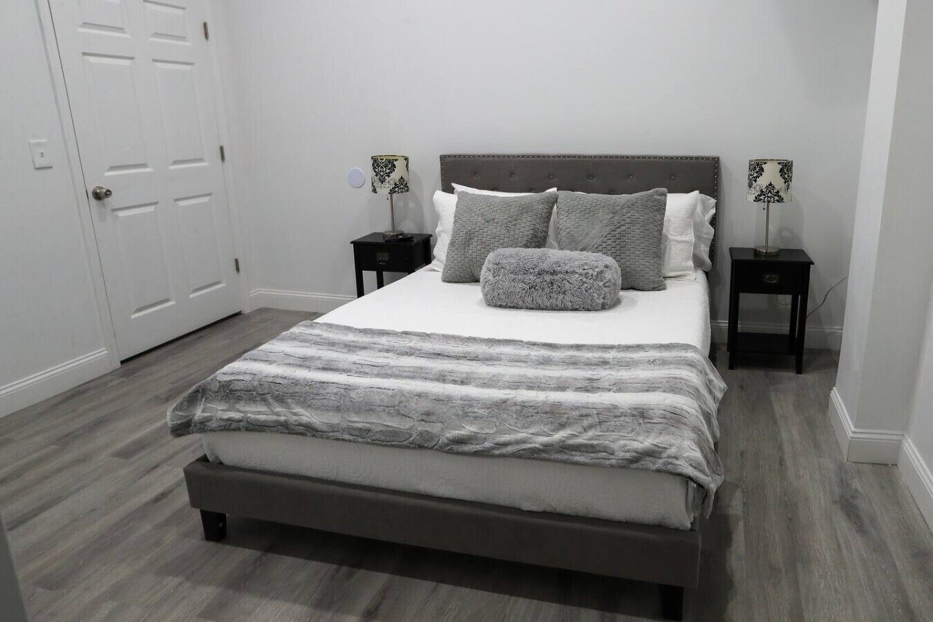 Ein Schlafzimmer mit einem Bett, zwei Nachttischen, einer Kopfteil und einer Tür.