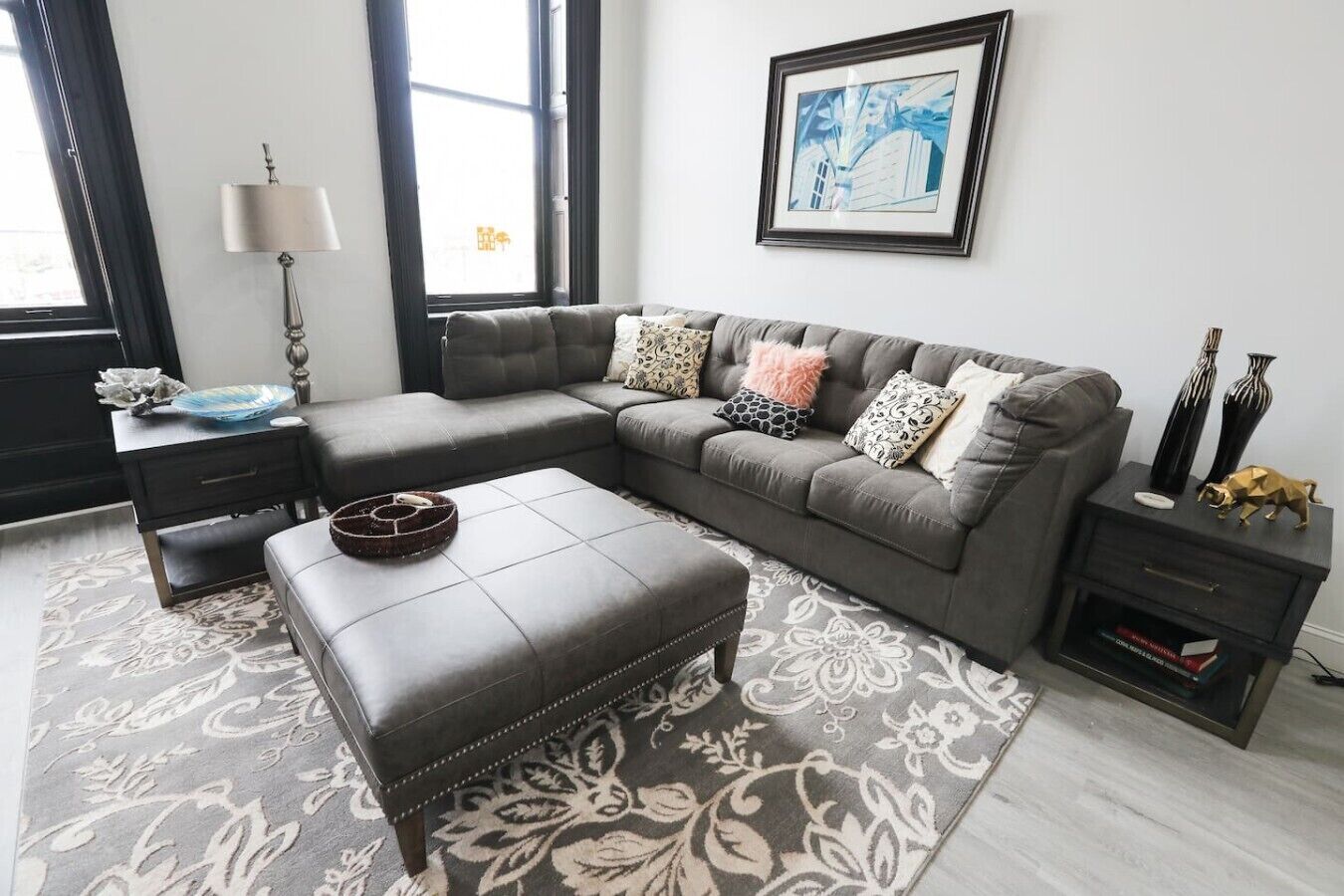 A modern living room with a sectional sofa, a matching ottoman, a side table, and a floor lamp.