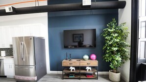 A modern kitchen with a stainless steel refrigerator, a wooden cabinet, a wall-mounted TV, and a potted plant.