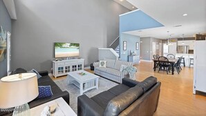 A modern living room with a sofa, coffee table, and TV, leading to a dining area with a table and chairs.
