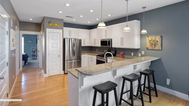 A modern kitchen with white cabinets, stainless steel appliances, a granite countertop, and pendant lighting.