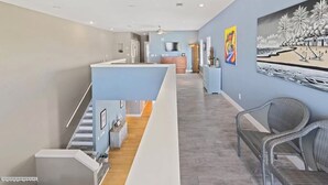 A modern interior with a staircase leading to a second floor, a dining area with a high table, and a wall with a large abstract painting.