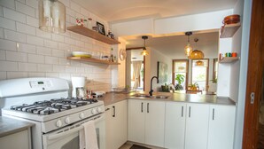 Una cocina moderna con armarios blancos, estufa a gas y un lavamanos. Hay repisas con vajilla y un reloj en la pared.