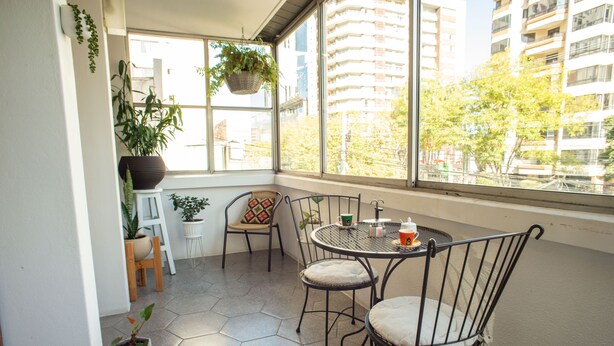 Una habitación soleada con un gran ventanal, una mesa redonda, dos sillas y varias plantas en macetas.