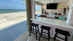A modern kitchen with a large window overlooking a beach, a flat-screen TV mounted above the counter, and a neon sign reading "TIKI BAR". - Panoramic view of the sugar white sand and the sparkling Emerald waters (Port St. Joe)