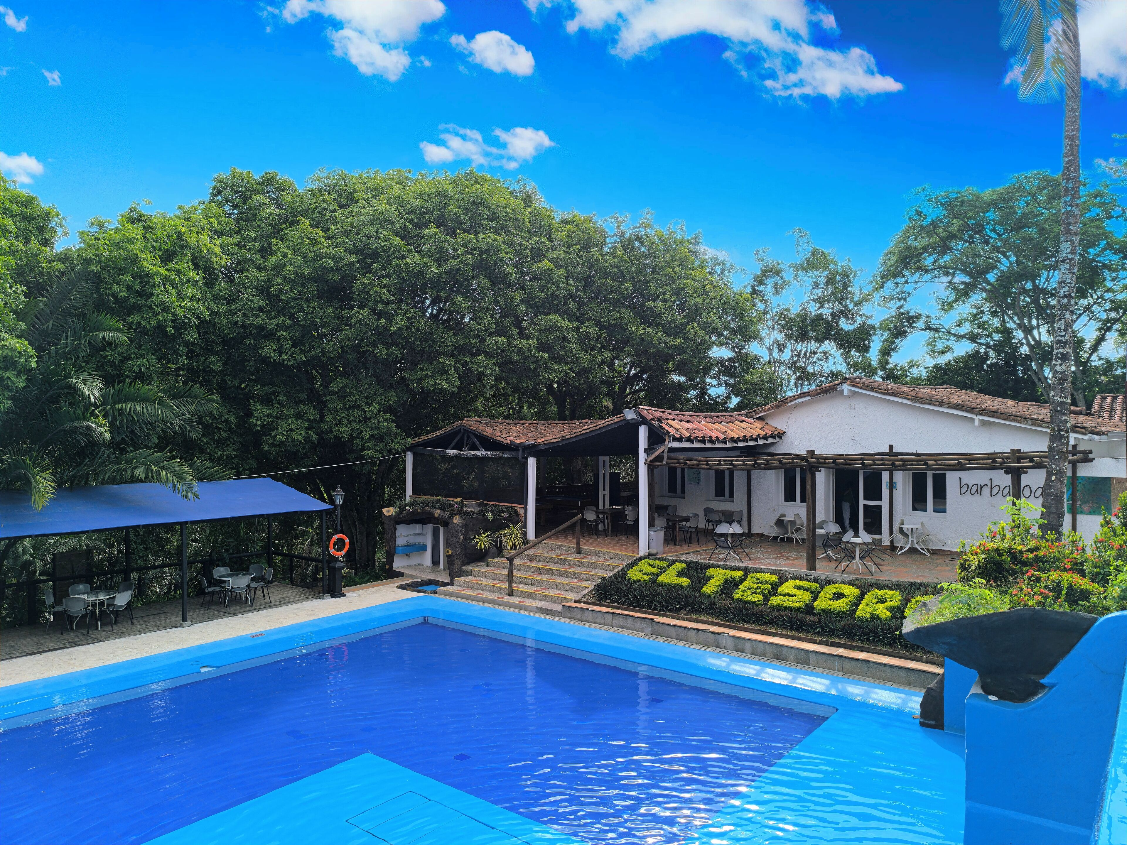 Una piscina con borde azul, rodeada de asientos al aire libre y un patio cubierto.