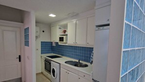 Una cocina compacta con muebles blancos, microondas integrado, lavadora y refrigerador.