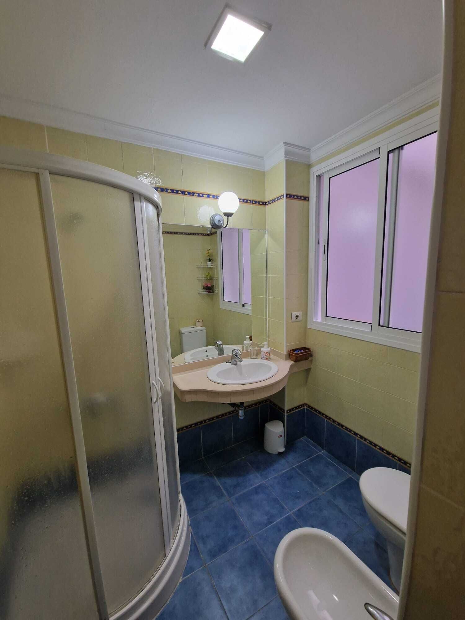 A bathroom with a shower, sink, toilet, and a window.
