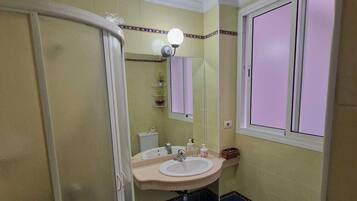 A bathroom with a shower, sink, toilet, and a window.