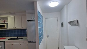 Una cocina compacta con armarios blancos, un salpicadero de azulejos azules, una puerta blanca y una pequeña encimera con un lavamanos.