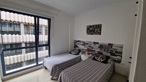 Un dormitorio con dos camas, una ventana con persianas, suelo de baldosas y una obra de arte en la pared.