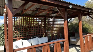 A wooden pergola with a lattice screen, wicker furniture, and a ceiling fan.