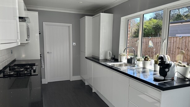 A modern kitchen with white cabinets, a black countertop, and a window overlooking a wooden fence.