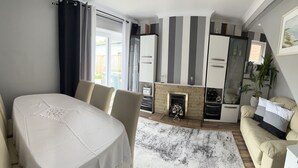 A modern living room with a fireplace, a dining area with a table set for four, and a kitchen with striped walls.