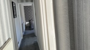 A narrow hallway with a radiator on the left, a patterned wall in the center, and a door on the right.