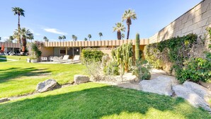 A courtyard with a pool, palm trees, and a building with a flat roof and large windows.