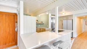 A modern kitchen with a central island, bar stools, and a wooden door.