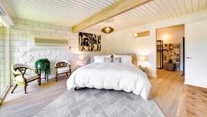 A bedroom with a large bed, two chairs, a wooden ceiling, a wall-mounted air conditioner, and a painting.