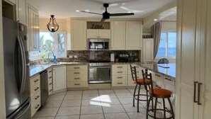 Una cocina moderna con gabinetes blancos, un refrigerador de acero inoxidable, un microondas y un ventilador de techo.