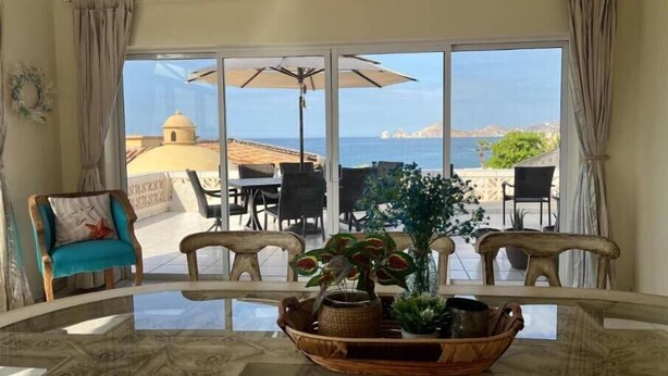 Comedor con mesa de vidrio, sillas y vista al mar.