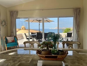 Comedor con mesa de vidrio, sillas y vista al mar.