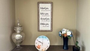 Una pared con una cita inspiradora enmarcada, un reloj decorativo, un florero con flores y una pequeña planta en maceta.