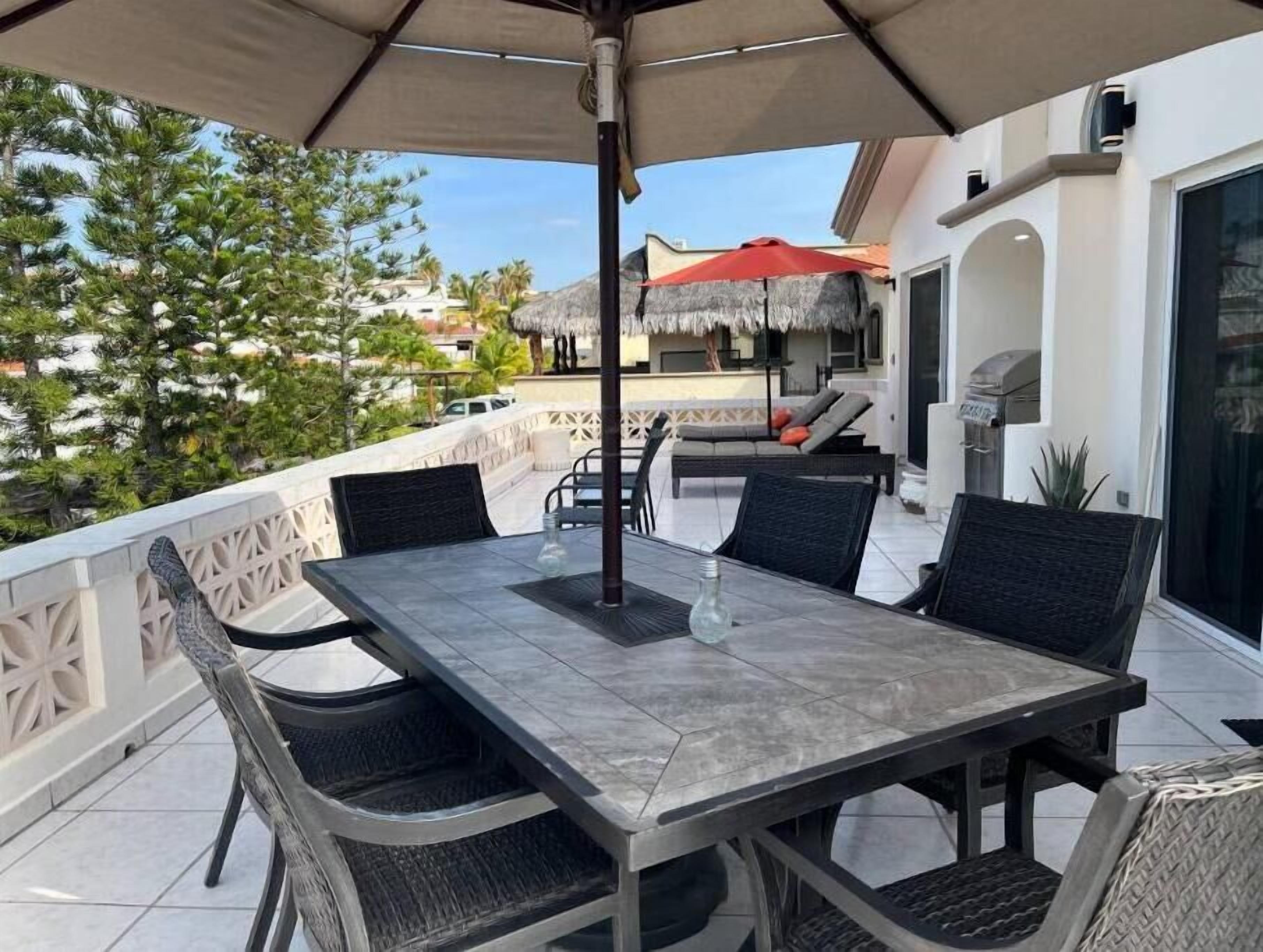 Une terrasse avec une table et des chaises, un barbecue et un parasol en chaume.