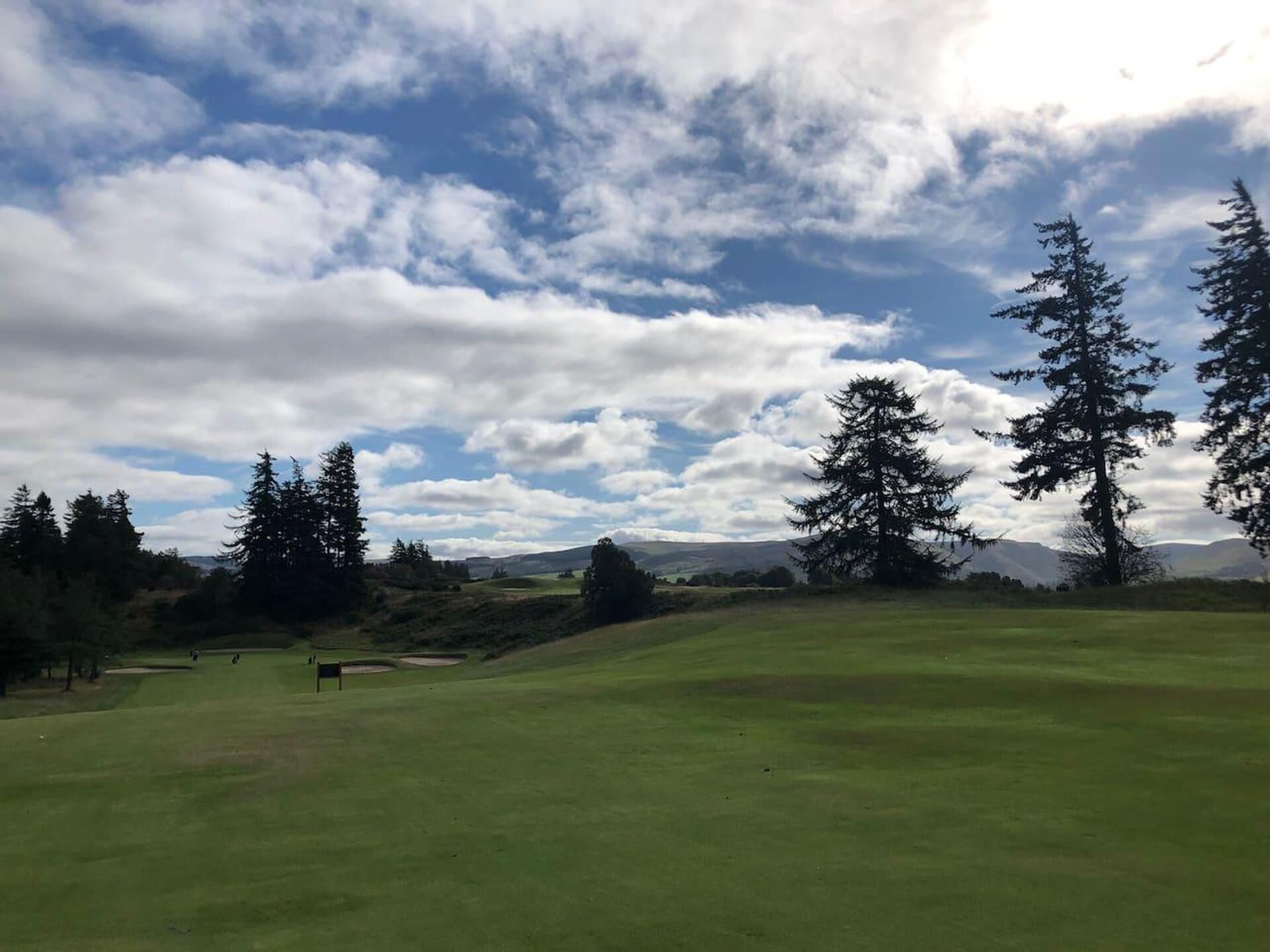 A golf course with a clear sky, trees, and distant hills.