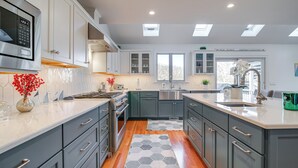 A modern kitchen with grey cabinets, a stainless steel range hood, and a large island with a sink. - Spacious home for entertaining, centrally located to beach, ferry, and airport. (Edgartown)