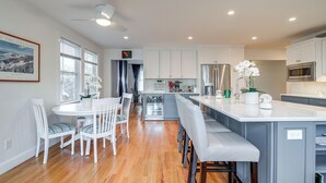 A modern kitchen with white cabinets, a central island, and a dining area with white chairs. - Spacious home for entertaining, centrally located to beach, ferry, and airport. (Edgartown)