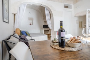 A cozy room with a bed, a dining table with a bottle of wine, a bowl of snacks, and a glass of wine.