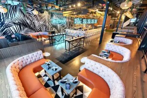 Uma área de estar moderna com assentos curvos, mesas e um bar ao fundo.
