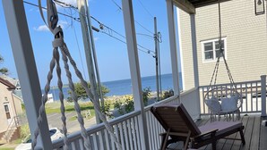 A wooden deck with two lounge chairs and a macrame hanging chair overlooking a body of water. - Brand new house with water views just steps from beach! (Milford)