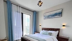 A bedroom with a bed, a nightstand, a wall-mounted light, a window with curtains, and a painting on the wall. - Elite Signature (Nairobi)