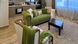 A modern living room with a green sofa, a coffee table, and a kitchen in the background. - Elite Signature (Nairobi)