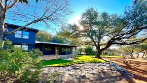 A modern house with a blue exterior, a well-maintained lawn, and a large tree in the foreground.