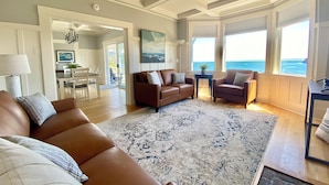 A spacious living room with a large brown leather sofa, a patterned rug, and a view of the ocean through large windows. - Amazing Views and Walkable to Downtown! Historic 3/2 Home, Sleeps 8 (Tiburon)