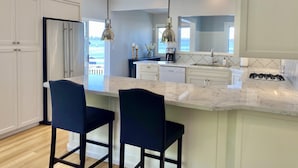 A modern kitchen with white cabinets, a marble countertop, two bar stools, and pendant lights. - Amazing Views and Walkable to Downtown! Historic 3/2 Home, Sleeps 8 (Tiburon)