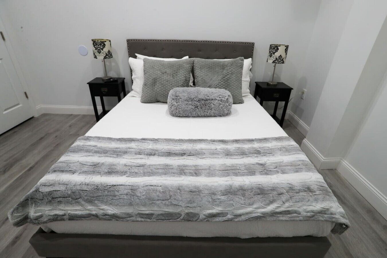 A bed with a grey and white patterned bedspread, two bedside tables with lamps, and a grey headboard.
