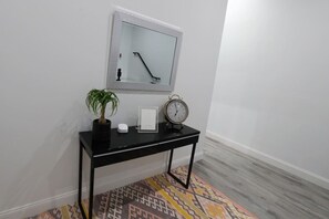 Une console noire sur laquelle sont posés un pot de fleurs, une horloge et un objet encadré, le tout adossé à un mur blanc.
