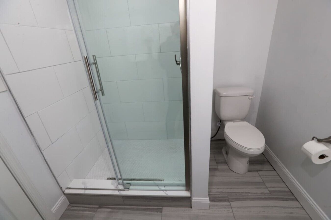A bathroom with a glass-enclosed shower, a toilet, and a roll of toilet paper on the wall.