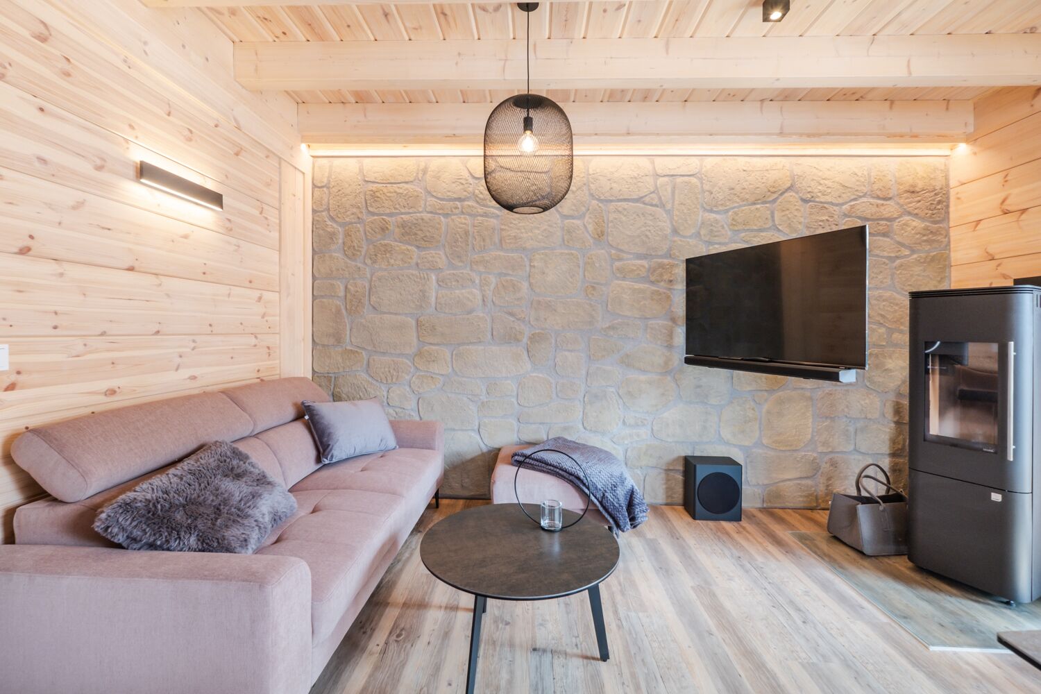 A cozy living room with a stone wall, a flat-screen TV, a sofa, a coffee table, and a fireplace.