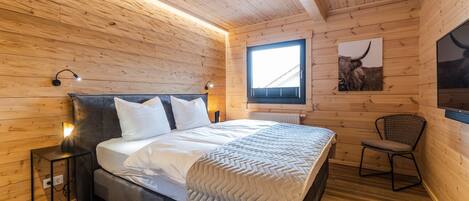 A wooden-paneled bedroom with a bed, a chair, a window, and a wall-mounted TV.