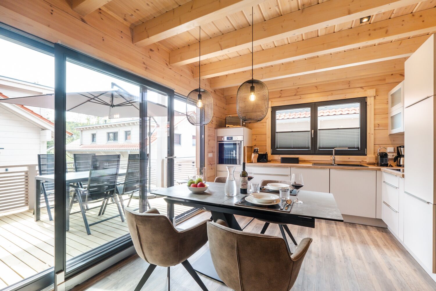 A modern kitchen with wooden beams, large windows, and a dining area with two chairs.