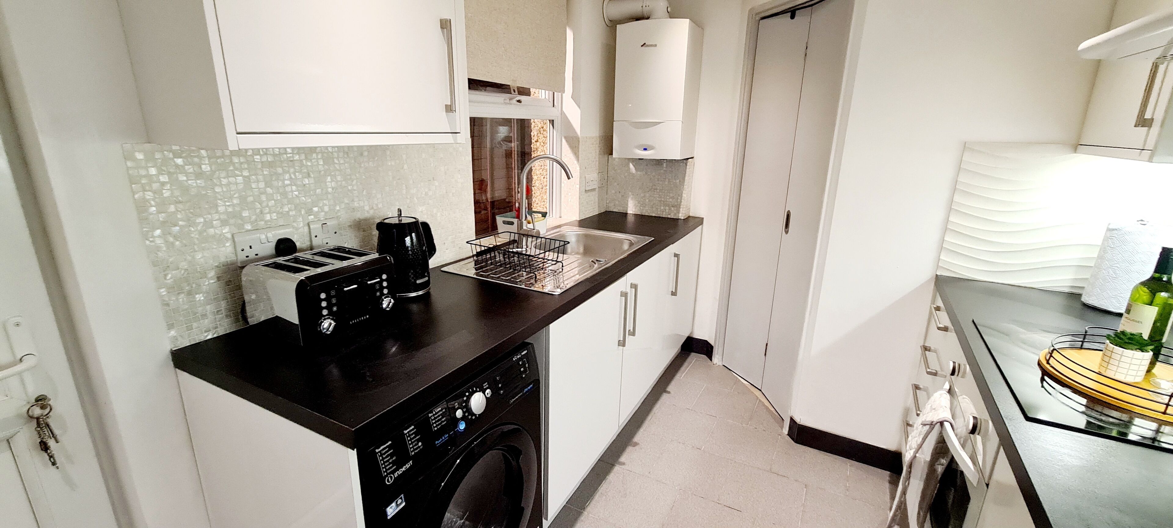 Een kleine keuken met een wasmachine, een koffiezetapparaat en een spoelbak.