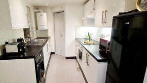 A compact kitchen with a washing machine, a microwave, and a refrigerator. - Maple House - Inviting 1-bed Apartment in London (London)